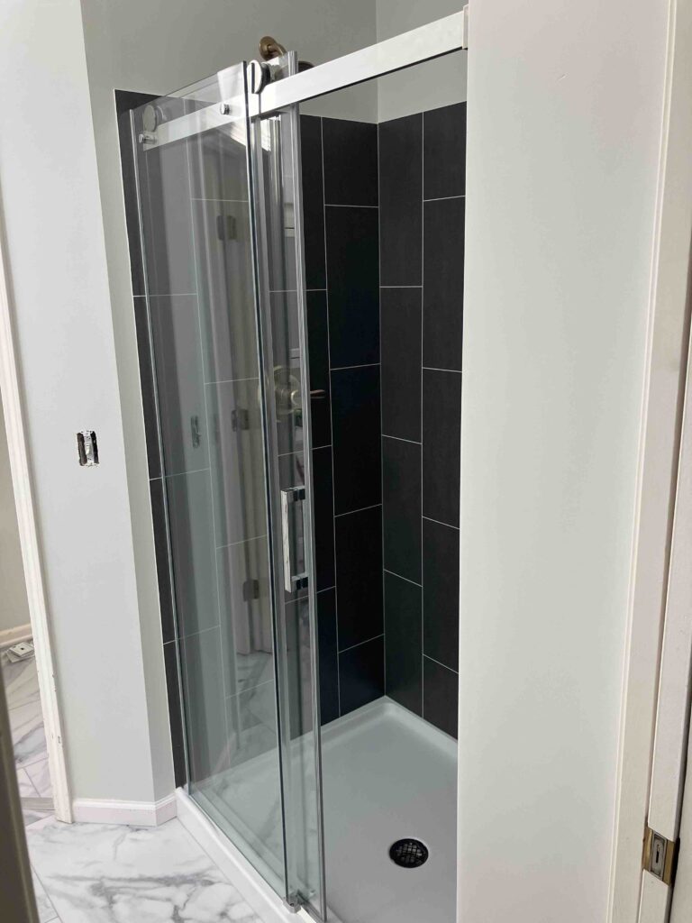 Walk-in shower with modern black tile and sliding glass shower door.