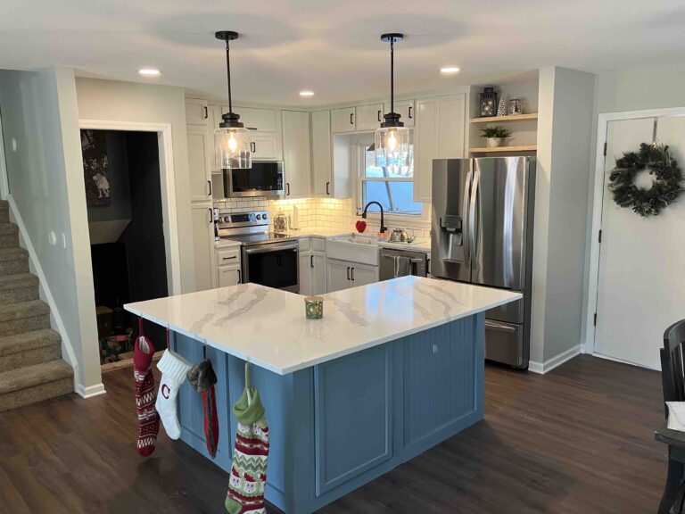 Remodeled, modern kitchen with white countertops, new LVT flooring, white cabinets, a blue island, and stainless steel appliances.