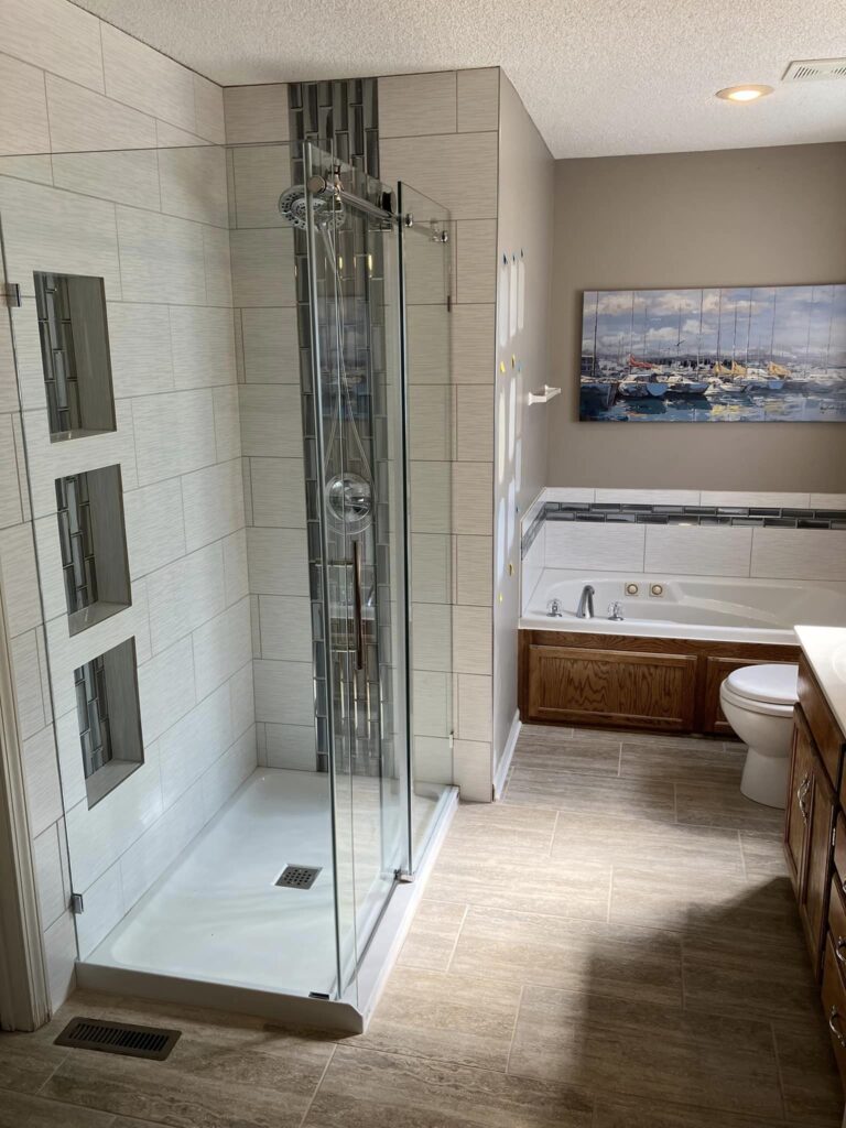 Renovated primary bed bathroom with modern tile in the shower and tub area and sleek sliding glass door, in Kansas City, MO.